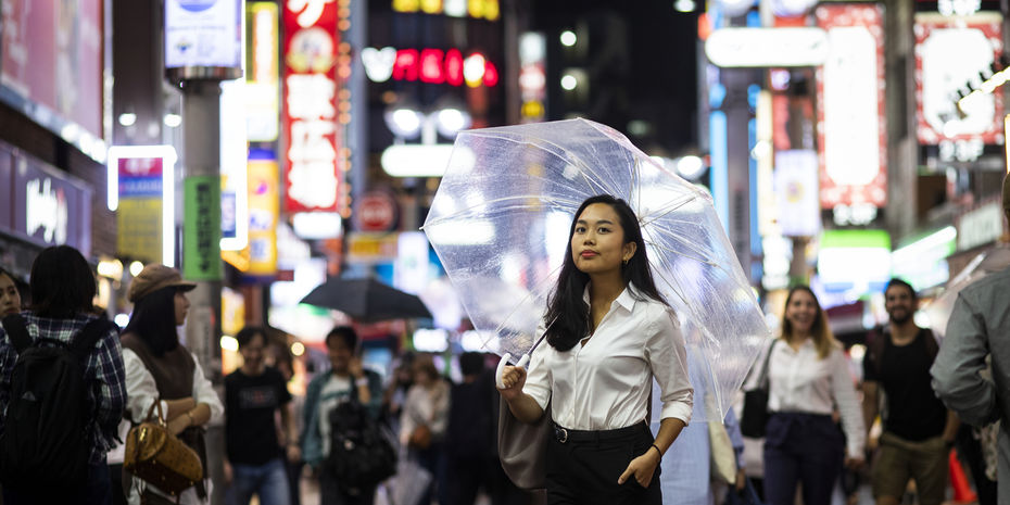 A Temple student stands on a busy street in Tokyo while holding an umbrella.