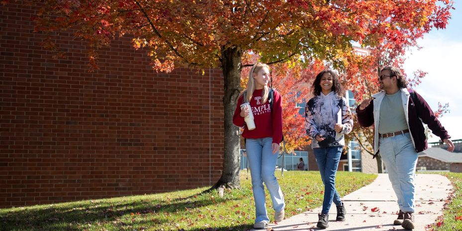 three students walking across Temple Ambler Campus on a fall day.