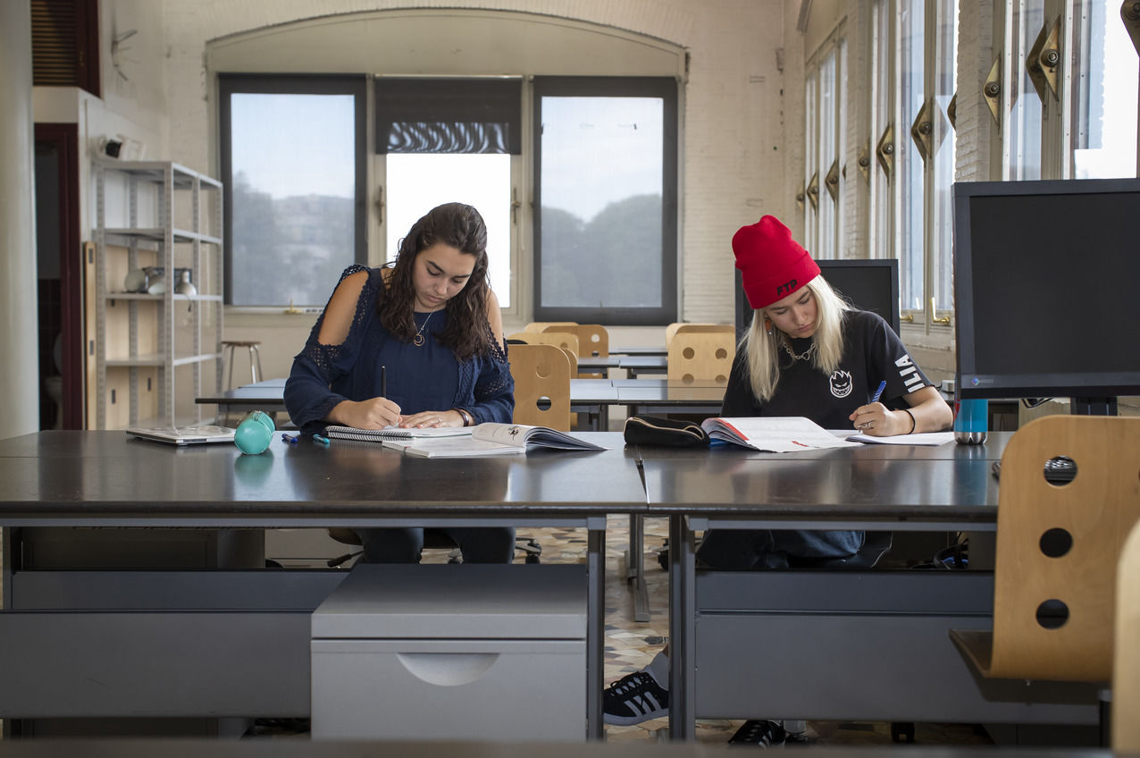 Two students sitting at a table writing in their notebooks in a study space at Temple Rome’s campus. 