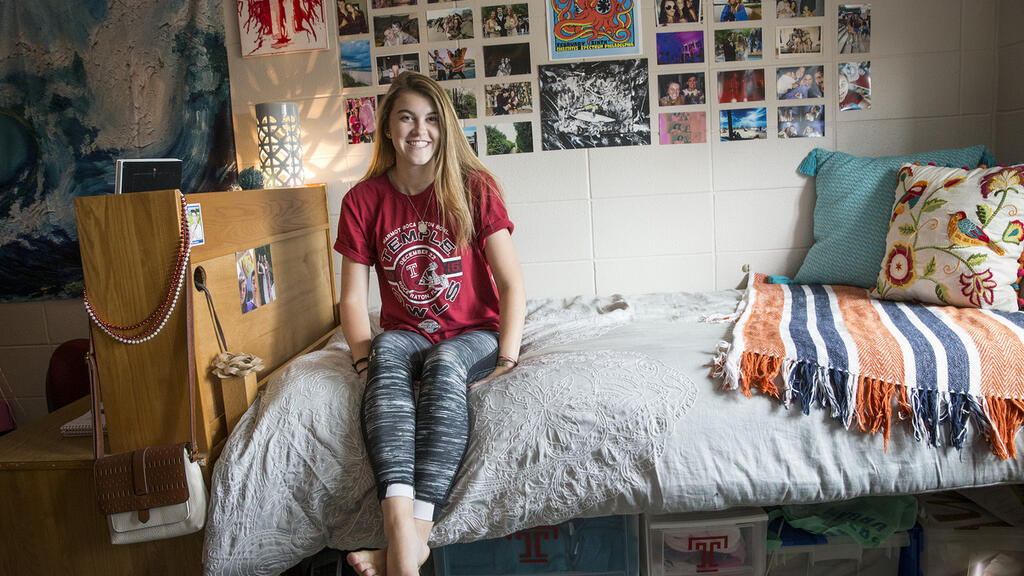 student sitting on her bed in her dorm room.