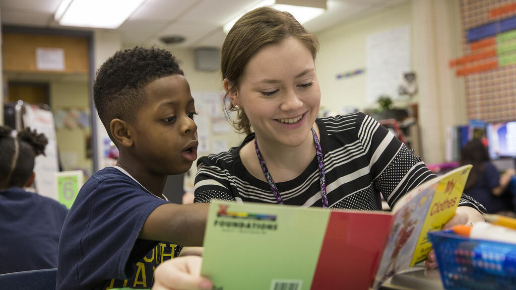 student teacher reading a book with an elementary school student.