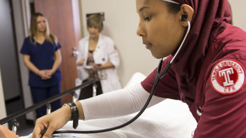 Student practicing with stethoscope on fake patient 
