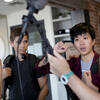 Four students stand around a digital camera. They seem to be setting up the camera for a project.