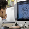 A male pre-college student faces a computer screen and works on creating digital artwork.