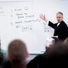 Professor lecturing at white board. 