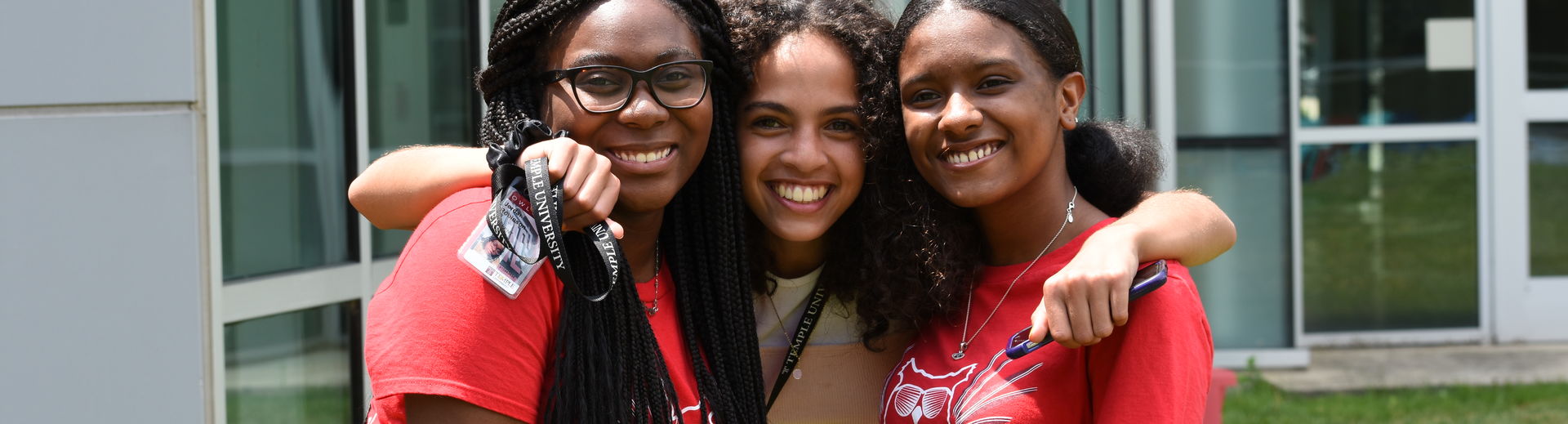 Three female pre-college students stand together with their arms around each other, posing for a photo.