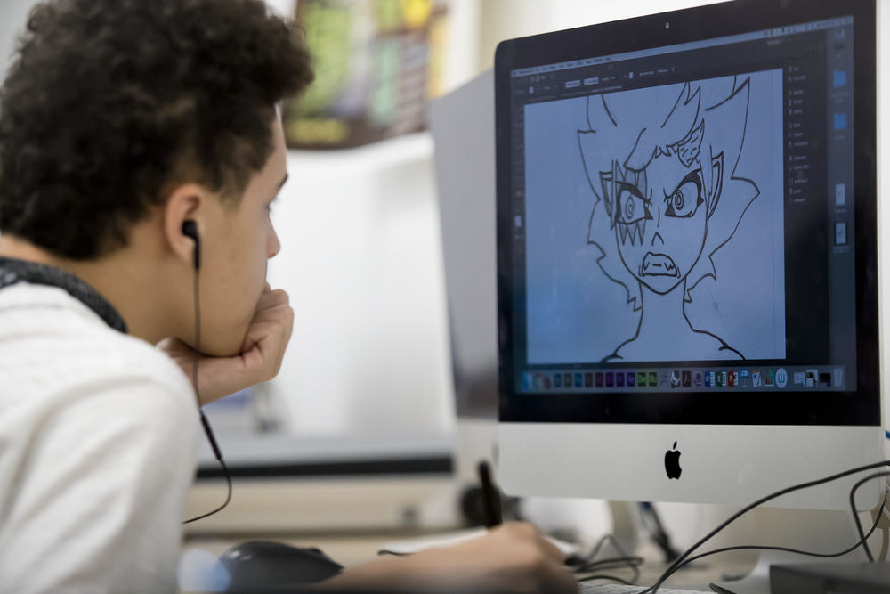 A male pre-college student faces a computer screen and works on creating digital artwork.
